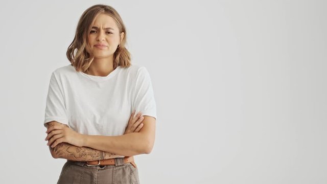 Disappointment young woman wearing basic t-shirt standing with arms folded feeling distaste isolated over white background