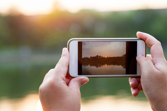 Hands holding smart phone taking photo of evening sunset landscape
