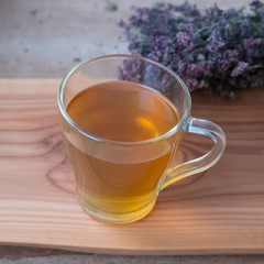 Warm oregano tea in a glass cup on wooden board