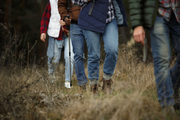 Group of friends on a camping or hiking trip in autumn day. Men and women with touristic backpacks going throught the forest, talking, laughting. Leisure activity, friendship, weekend.