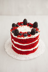 homemade red velvet cake decorated with berries on a light wooden background