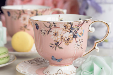 Pink tea cups with floral ornament and macaroon sweets