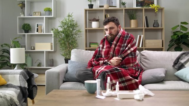 A sick man is measuring the temperature at home on the sofa