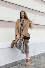 brown fur coat faux fur, long leopard print dress, warm uggs, shoulder bag, beautiful European model girl with long hair posing fun outdoors near the wall