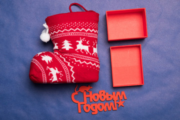Naklejka premium Christmas background with the inscription in Russian New Year's studio image. Red gift box with christmas sock on a blue background. Greeting Christmas card.