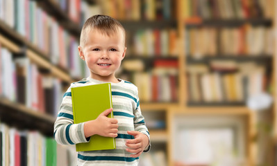 reading, education and childhood concept - portrait of smiling little boy holding book over library...