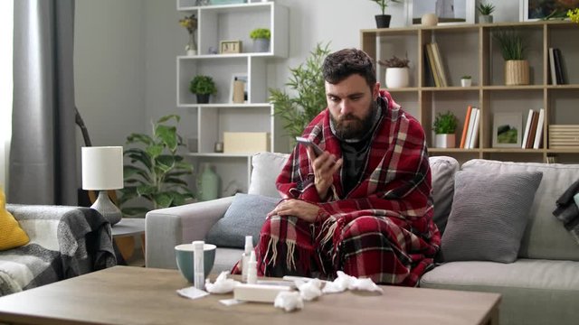 Ill man uses a smartphone at home on the sofa
