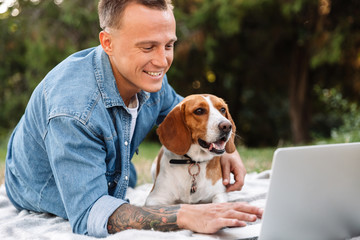 Photo of young man in park with his canine dog and laptop computer
