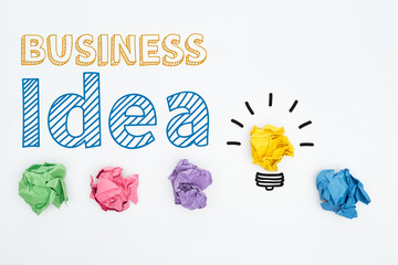 top view of business idea inscription near colorful crumpled paper balls on white background, business concept