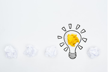 top view of white and yellow crumpled paper balls and illustration of light bulb on white background, business concept