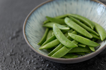 vegetable, food and culinary concept - close up of peas in bowl on wet slate stone background