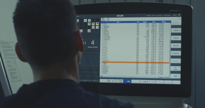 mechanical technician operative of cnc milling cutting machine working at computer at tool workshop, looks into the monitor