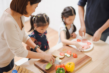 Young Asian love family are preparing the breakfast, sandwich vegetable on table in the kitchen which Excited smiling and felling happy. parent teach daughter to cooking food on the day at home.