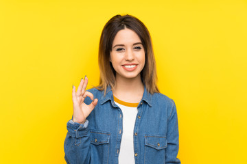 Young woman over yellow background showing an ok sign with fingers