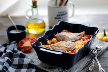 Chicken fillet baked with peppers in a blue ceramic dish on a wooden table