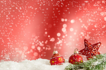 Fototapeta na wymiar Rote Christbaumkugeln liegen im Schnee vor einem rotem Hintergrund mit bokeh.