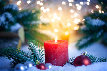 Weihnachtsdekoration mit einer brennenden roten Kerze, Tanne, Kugeln und Schnee.