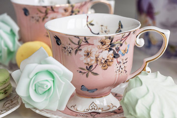 Pink tea cups with floral ornament and macaroon sweets