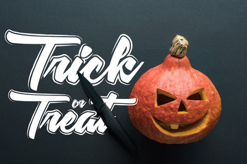 top view of carved spooky Halloween pumpkin with knife on black background with trick or treat illustration