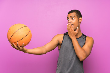Young sport man with ball of basketball over isolated purple wall with surprise and shocked facial expression