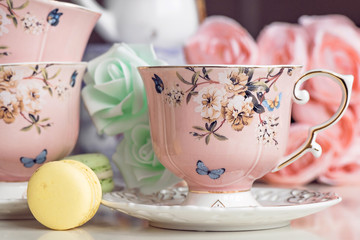 Pink tea cups with floral ornament and macaroon sweets