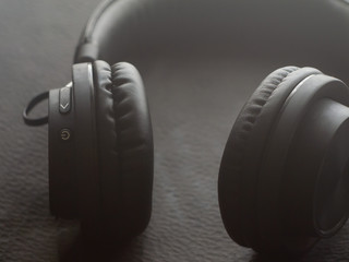 Black wireless headphones on a black textured background. Close up.