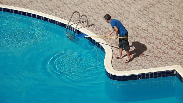 Male worker cleaning outdoor pool with scoop net