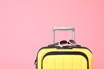Yellow suitcase with sunglasses on pink background. Space for text