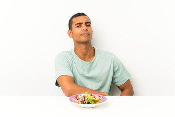 Young handsome man with salad in a table standing and looking to the side