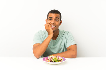 Young handsome man with salad in a table nervous and scared