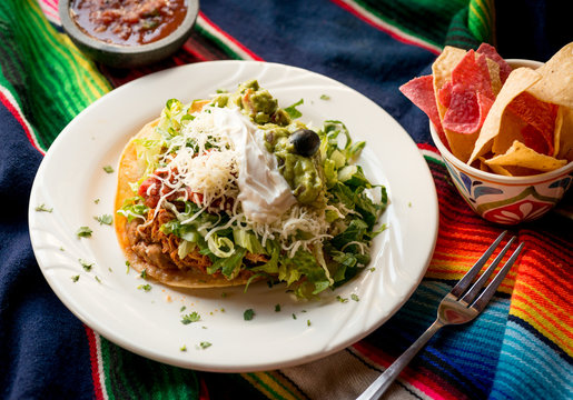 Crispy tortilla tostada with chicken, beans, lettuce, cheese, guacamole, sour cream, and salsa. Served with chips and dipping salsa styled on a sarape.