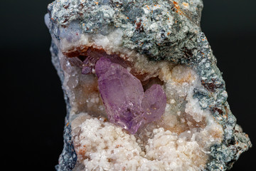 macro mineral amethyst stone in rock on a black background