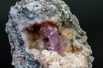 macro mineral amethyst stone in rock on a black background