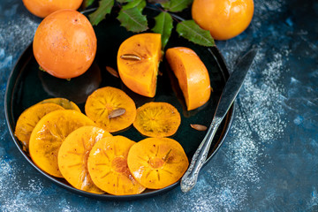 Persimmon on a dark, stone background. Near the berries of viburnum. Winter fruit. Healthy eating Orange color. Copy space.  