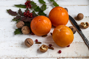 Persimmon on a light, wooden background. Near walnuts, viburnum berries. Winter fruit. Healthy eating Orange color. Copy space. 