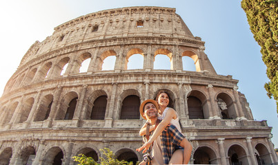 Young happy couple having fun at Colosseum, Rome. Piggyback posing for pictures. - obrazy, fototapety, plakaty