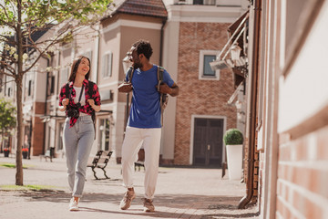 full length shot of multiracial couple of tourists walking no the city and talking