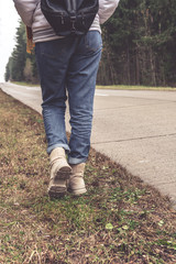 Female teen traveler hitchhiking along the road with a backpack in the warm autumn. The concept of a cozy outdoor activity