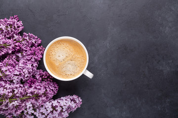Cup of morning coffee with spring lilac flowers branches blossoming on black stone background Top view