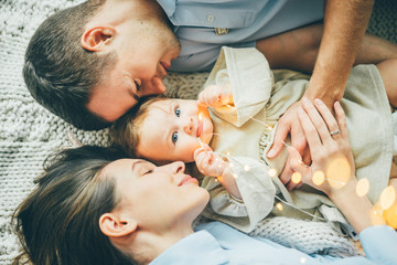 Young parents and cute baby lying together. Young parents holding hands together and smile. Top...