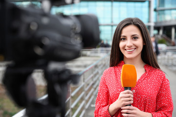 Young female journalist with microphone working on city street