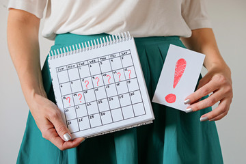 Woman holding calendar with marked missed period and exclmation mark. Unwanted pregnancy and delay in menstruation. - obrazy, fototapety, plakaty
