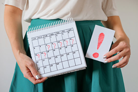 Woman holding calendar with marked missed period and exclmation mark. Unwanted pregnancy and delay in menstruation.