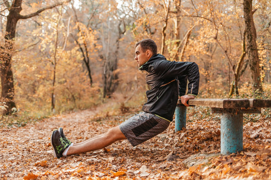 Concept of sport and active lifestyle. A young man in a black tracksuit push-ups from the bench, in the autumn Park. Profile view