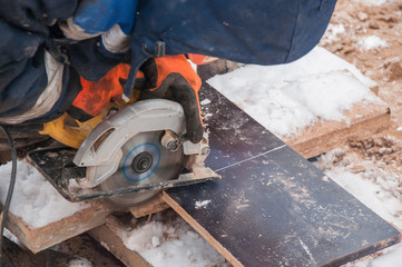 A worker cuts off part of a laminated board with a circular saw.