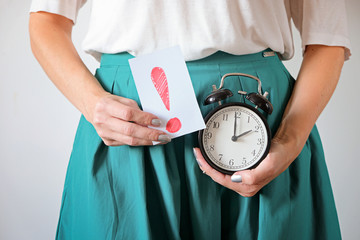 Woman holding clock at belly. Missed period, unwanted pregnancy and delay in menstruation.