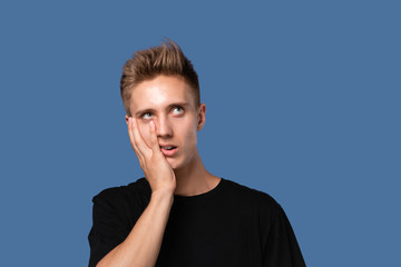 Tired young man in a black t-shirt holding hand on head covering face isolated over grey nackground