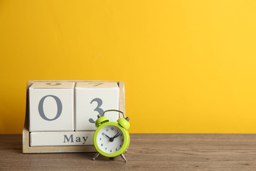 Wooden block calendar and alarm clock on table against yellow background. Space for text