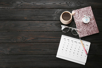 Flat lay composition with calendar and cup of coffee on black wooden table. Space for text