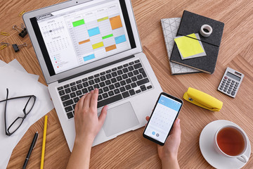 Woman using calendar on laptop and smartphone at wooden table, closeup